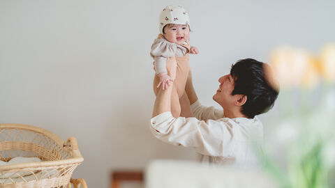 Ein Vater hält sein Baby mit beiden Händen hoch und lächelt es an Ein Vater hält sein Baby mit beiden Händen hoch und lächelt es an