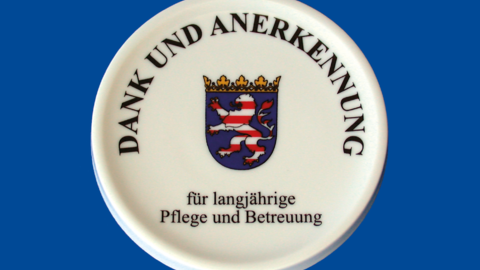 Pflegemedaille Weißer Kreis mit Hessenwappen in der Mitte auf blauem Hintergrund.