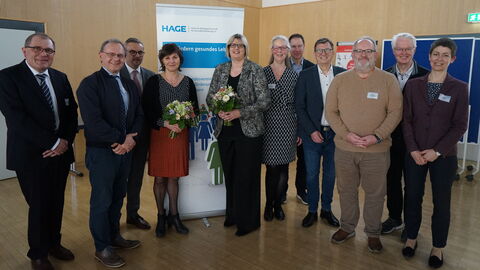 Dr. Sonja Optendrenk (Mitte rechts) gemeinsam mit weiteren Akteuren der HAGE e. V.  vor einem Aufsteller. Sie hält einen Blumenstrauß in Händen und alle lächeln in die Kamera.