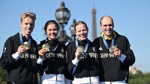 Vier Sportler stehen vor dem Eiffelturm in Paris und halten ihre Goldmedaillen in die Kamera.
