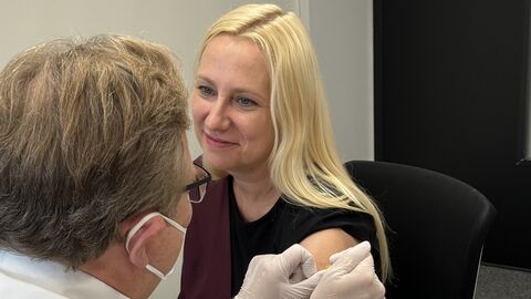 Gesundheitsministerin Stolz während der Grippeschutzimpfung Gesundheitsministerin Stolz sitzt auf einem Stuhl. Ein Arzt ist gerade dabei ein Pflaster auf ihren Oberarm zu kleben.