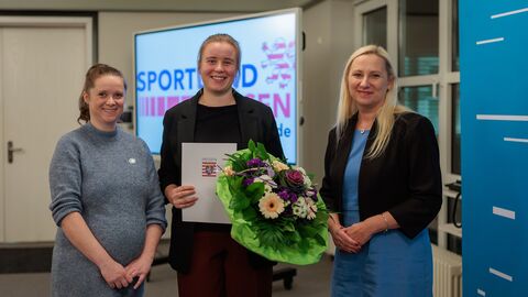 Julia Seiß von der Hessischen Ruderjugend. 3 Frauen stehen nebeneinander und halten Blumen und eine Urkunde hoch.