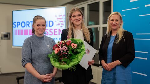 Luisa Schlüter von der Freien Turnerschaft Dörnigheim. 3 Frauen stehen nebeneinander und halten Blumen und eine Urkunde hoch.