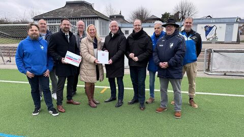 Mehrere Männer und eine Frau stehen auf Sportplatz. 