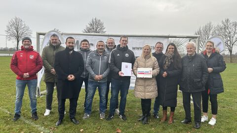 Zwölf Personen stehen nebeneinander auf einem Fußbaldfeld.