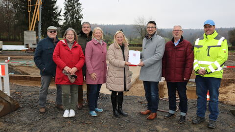 Eine Gruppe Personen steht an einer Baustelle im Freien, Sportministerin Stolz übergibt eine Urkunde.