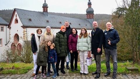 Mehrere Erwachsene und Kinder stehen vor einem alten Kloster. 