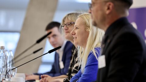 Vierte Konferenz zur Umsetzung der Krankenhausreform in Darmstadt Vier Personen sitzen an einem Tisch mit einem Mikrofon vor sich und sind von der Seite zu sehen.
