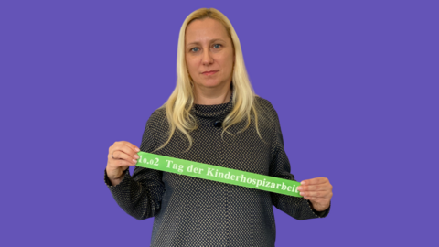 Familienministerin Diana Stolz hält ein grünes Band mit dem Aufdruck "10.02 Tag der Kinderhospizarbeit" in den Händen