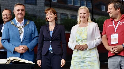 Drei Männer und zwei Frauen stehen auf der Bühne und lachen in Kamera.