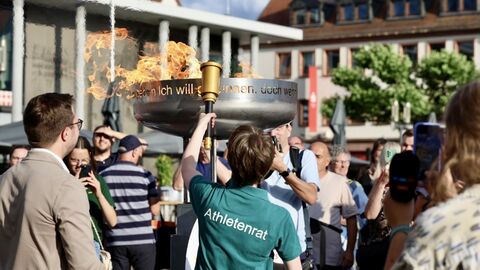 Mehrere Personen stehen um eine Feuerschale. Eine Person hat diese gerade entzündet- 