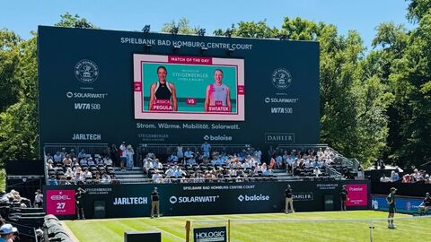 Tennisfeld mit Netz, im Hintergrund Publikum auf den Tribünen und eine digitale Anzeigetafel.