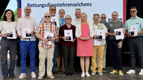 Gesundheitsministerin Diana Stolz steht mit den ausgezeichneten Rettungskräften auf einer Bühne.