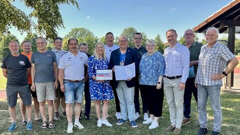 Stolz steht mit einer Gruppe von Menschen auf einer Wiese. Sie hält ein Schild in der Hand mit der Aufschrift "Sportland Hessen". 