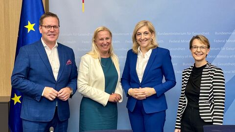 Vier Personen stehen nebeneinander vor einem Hintergrund vom Bundesministerium für Gesundheit.