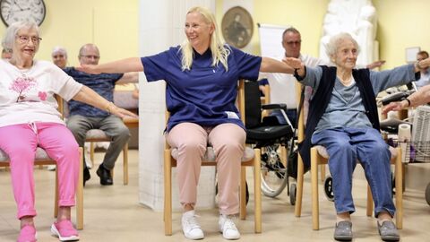 Mehrere ältere Person machen Gymnastik auf Stühlen.