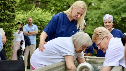 Zwei Personen halten Hände in Brunnen, andere stehen drum herum.
