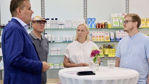 Personen stehen in Apotheke um einen Hochtisch herum und unterhalten sich.