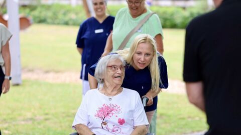 Gesundheitsministerin Diana Stolz schiebt eine ältere Dame die in einem Rollstuhl sitzt. 