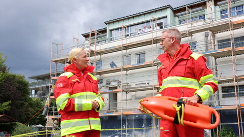 Präsident des DLRG LV Hessen Michael Hohmann und Ministerin Stolz mit Rettungsboje. Zwei Personen in roter DLRG Kleidung stehen vor einem Gebäude.