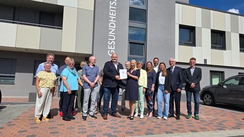 Gesundheitsministerin Stolz bei der Bescheidübergabe in Frankenau mit einer Gruppe vor einem Gebäude.