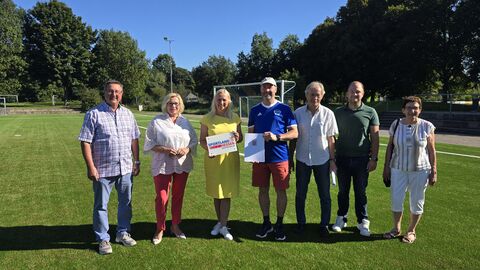 Mehrere Personen stehen auf Sportplatz. Im Hintergrund befindet sich ein Tor.