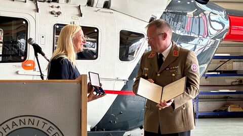 Gesundheitsministerin Diana Stolz und Prof. Dr. Simon Little bei der Verleihung des Verdientsordens vor einem Einsatzhubschrauber.