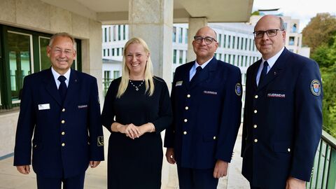 Gesundheitsministerin Stolz steht mit 3 Männern in Uniform zusammen und lächelt in Kamera.