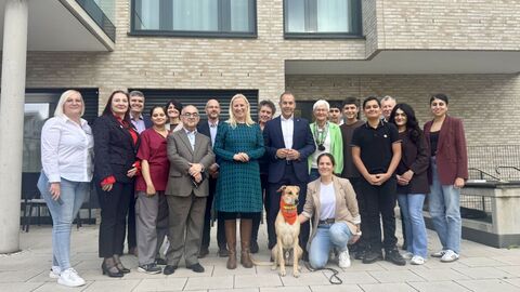 Mehrere Personen und ein Hund stehen vor Gebäude.