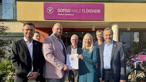 Mehrere Personen stehen vor Gebäude und halten Förderbescheid in den Händen.