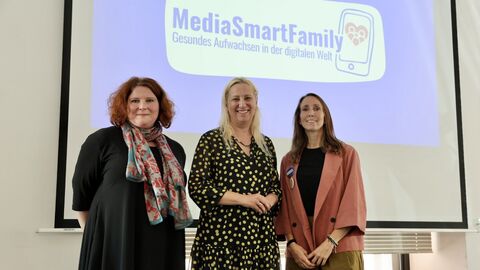 Familienministerin Stolz steht mit zwei weiteren Personen vor einem Smartboard mit einer Präsentation zum Thema "MediaSmartFamily".