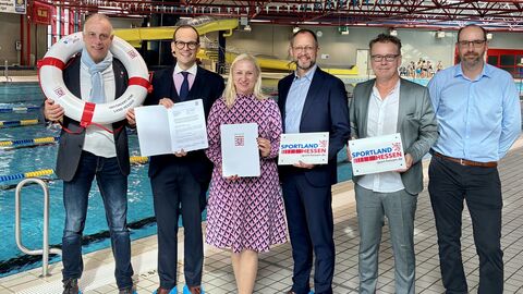 Mehrere Personen stehen mit Förderbescheiden in einem Schwimmbad.