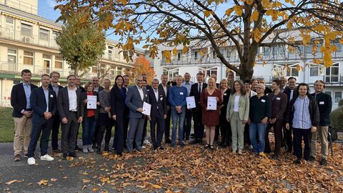 Eine Gruppe von ungefähr 30 Personen stehen unter einem herbstlichen Baum und halten teilweise Urkunden in den Händen.