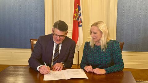 Ministerpräsident Rhein und Familienministerin Stolz sitzen an einem Tisch zur Unterzeichnung der Gesetzesänderung.