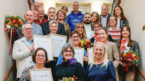 Eine Gruppe von Menschen stehen in einem Treppenhaus. Viele halten Blumensträuße oder gerahmte Urkunden in den Händen.