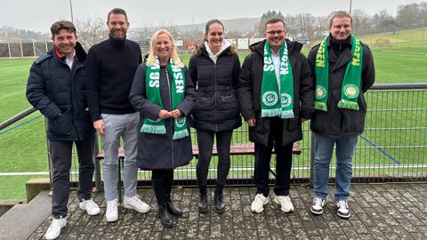 Diana Stolz steht mit 5 weiteren Personen in einer Reihe. Im Hintergrund sieht man ein Fußballfeld.