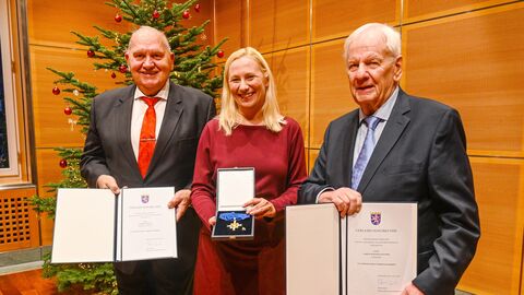 Diana Stolz hält einen Orden in den Händen und steht in der Mitte - links und rechts stehen jeweils zwei festlich gekleidete Herren und halten jeweils eine Auszeichnung in den Händen.