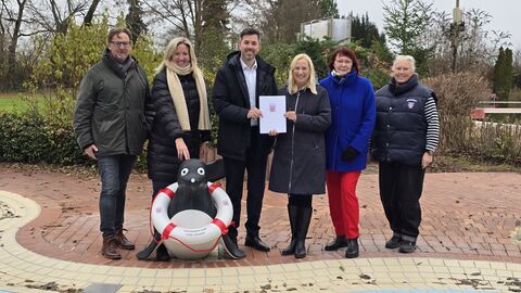 Fünf Personen stehen mit dicken Jacken im Freibad und halten eine Urkunde hoch.