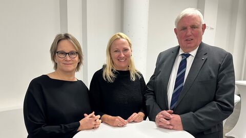 Zwei Frauen und ein Mann stehen zusammen an einem Stehtisch