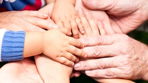 Mehrere Hände von Kindern und Erwachsenen liegen übereinander und symbolisieren Zusammenhalt, Unterstützung und Gemeinschaft.