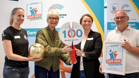 Drei Frauen und ein Mann stehen nebeneinander vor einem Aufsteller mit der Aufschrift "Safe Kids".