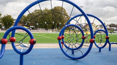 Blaues, rundes Klettergerüst. Im Hintergrund sieht man einen Fußballplatz